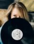 A woman partially hides her face behind a vintage vinyl record, adding a retro vibe.